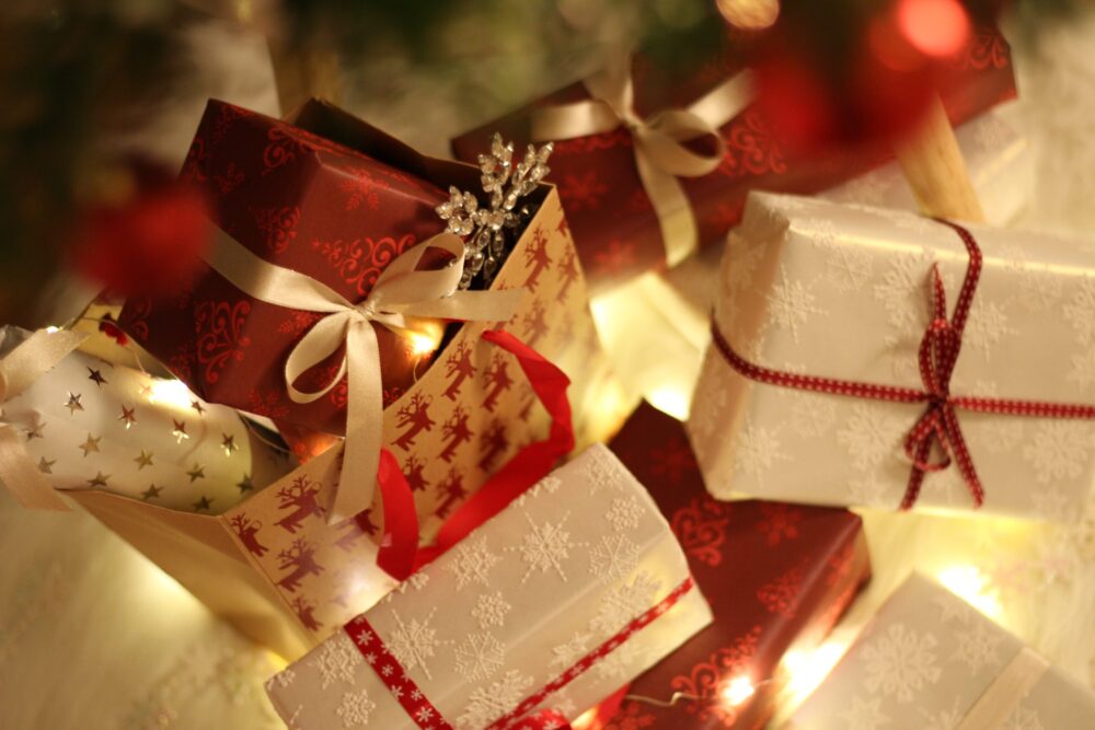 Small Christmas packages wrapped up in papers and string with twinkling lights in the background.